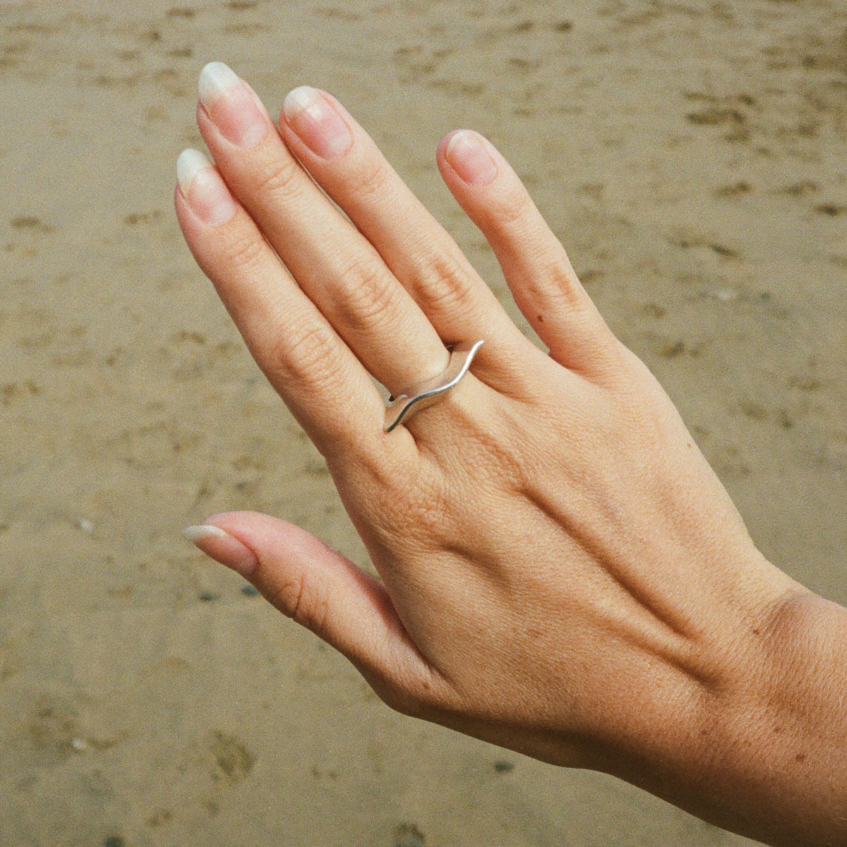 Silver wave ring worn on the hand on a Cornish beach