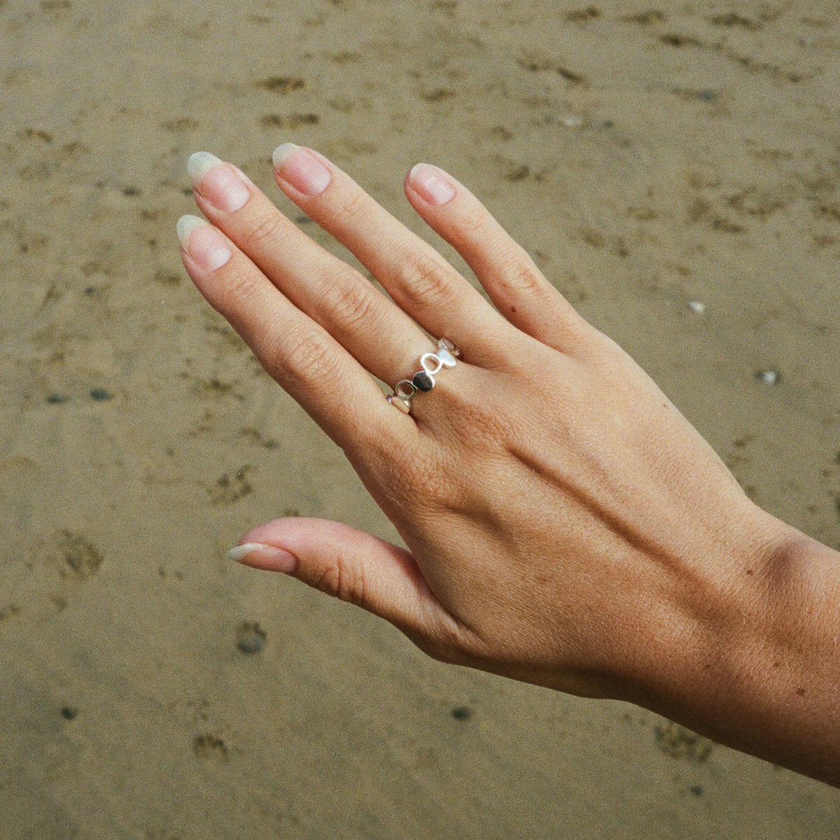 Silver pebble ring worn on the hand on a Cornish beach