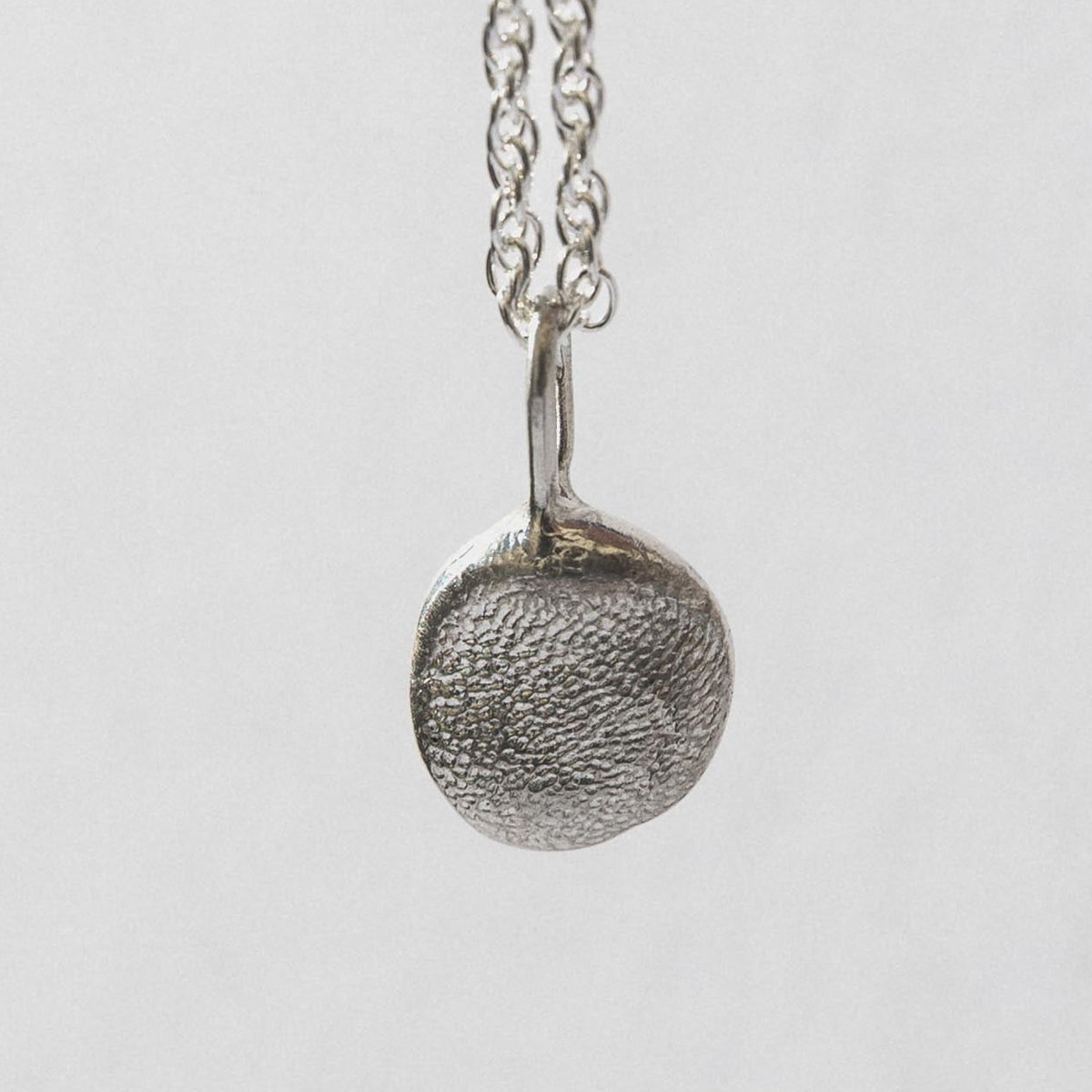 A gold-colored pendant with a pebble design is displayed on a white box with the brand name Kova.