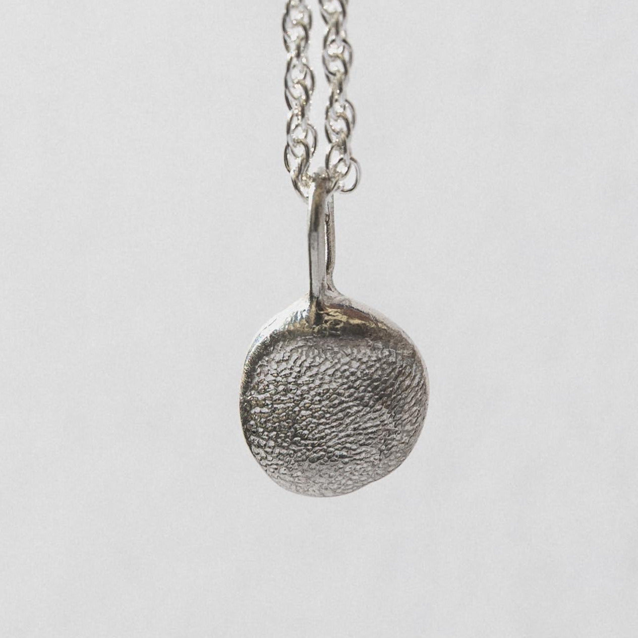 A gold-colored pendant with a pebble design is displayed on a white box with the brand name Kova.