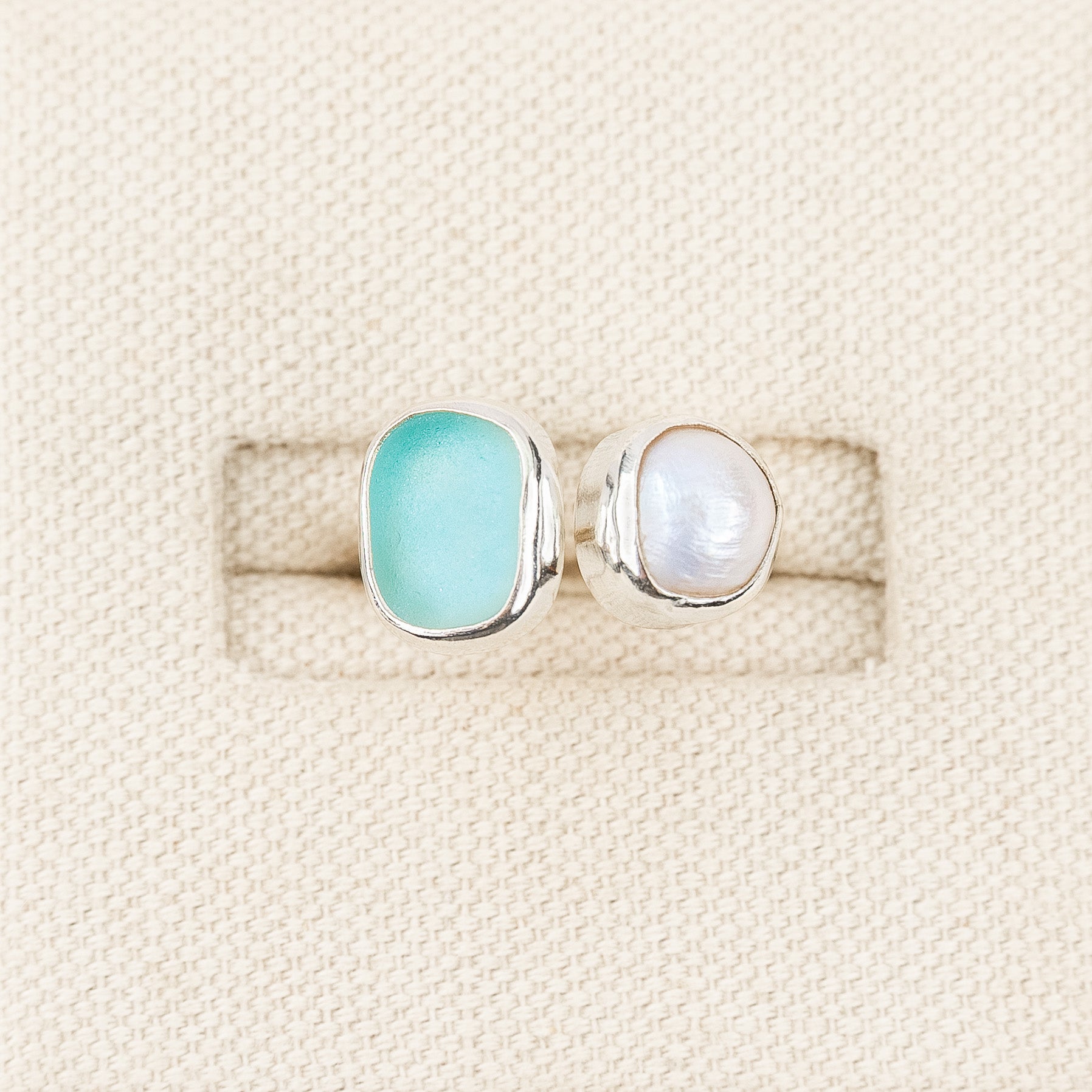 Two rings with turquoise and pearl-like stones on a textured beige background
