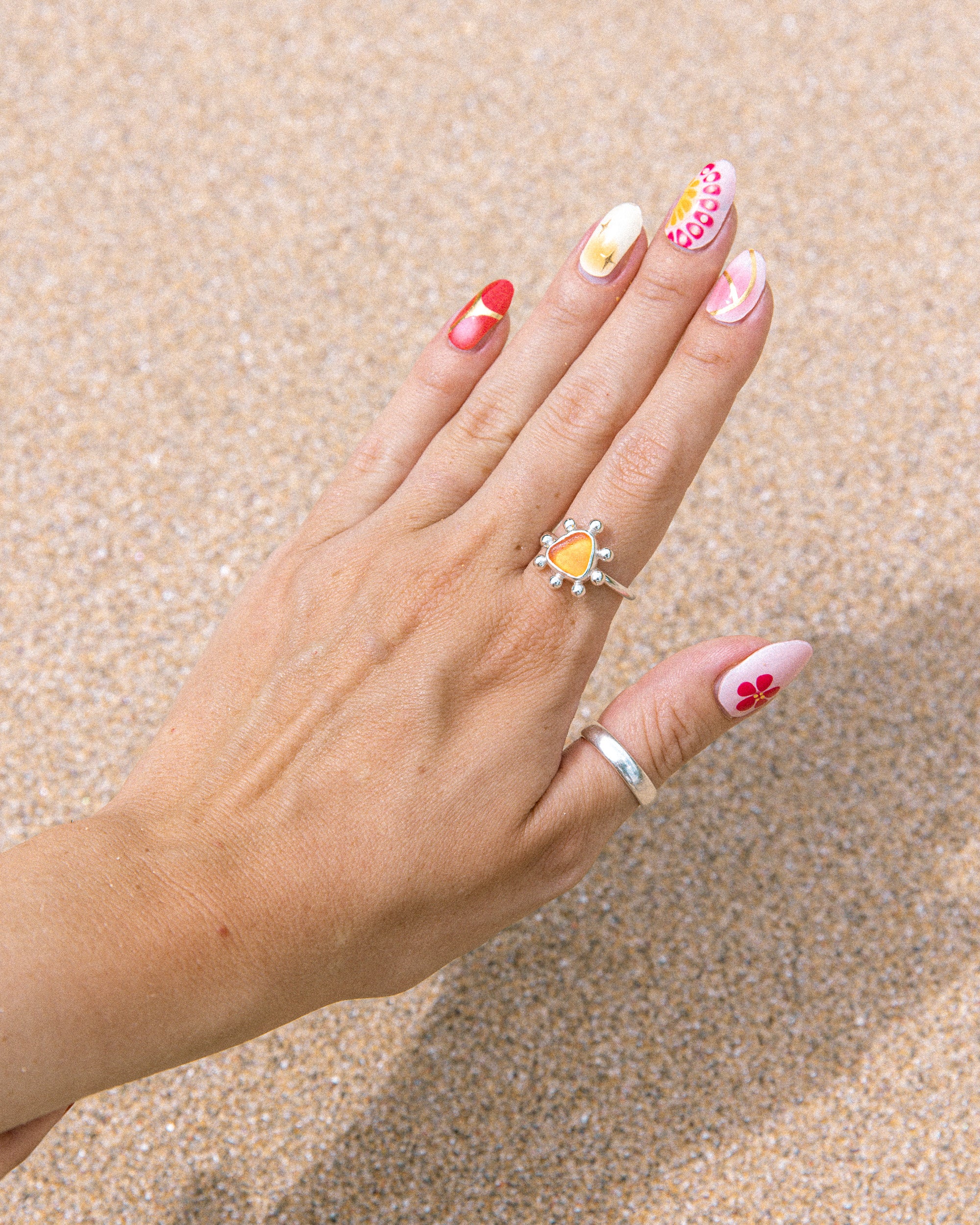 Orange sea glass ring worn on hand over wet Cornish sand, Broken Wave Jewellery