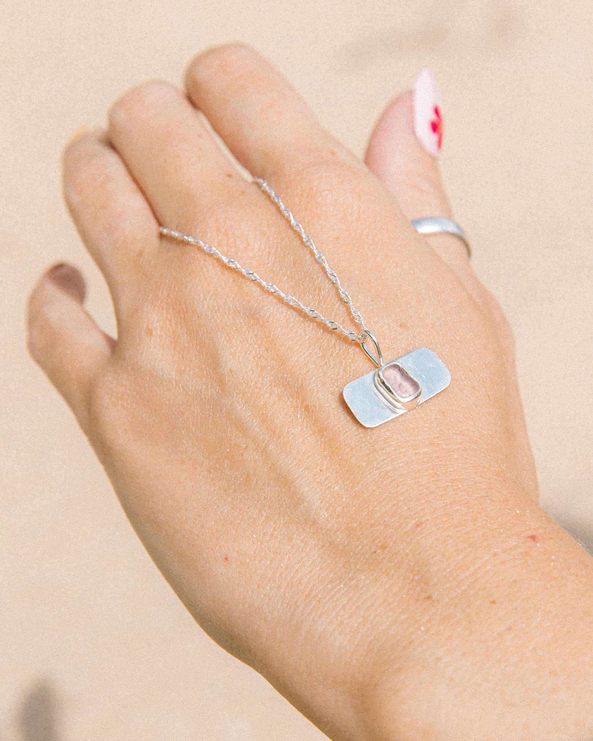Purple sea glass necklace worn on hand, handmade sterling silver, Broken Wave Jewellery Newquay
