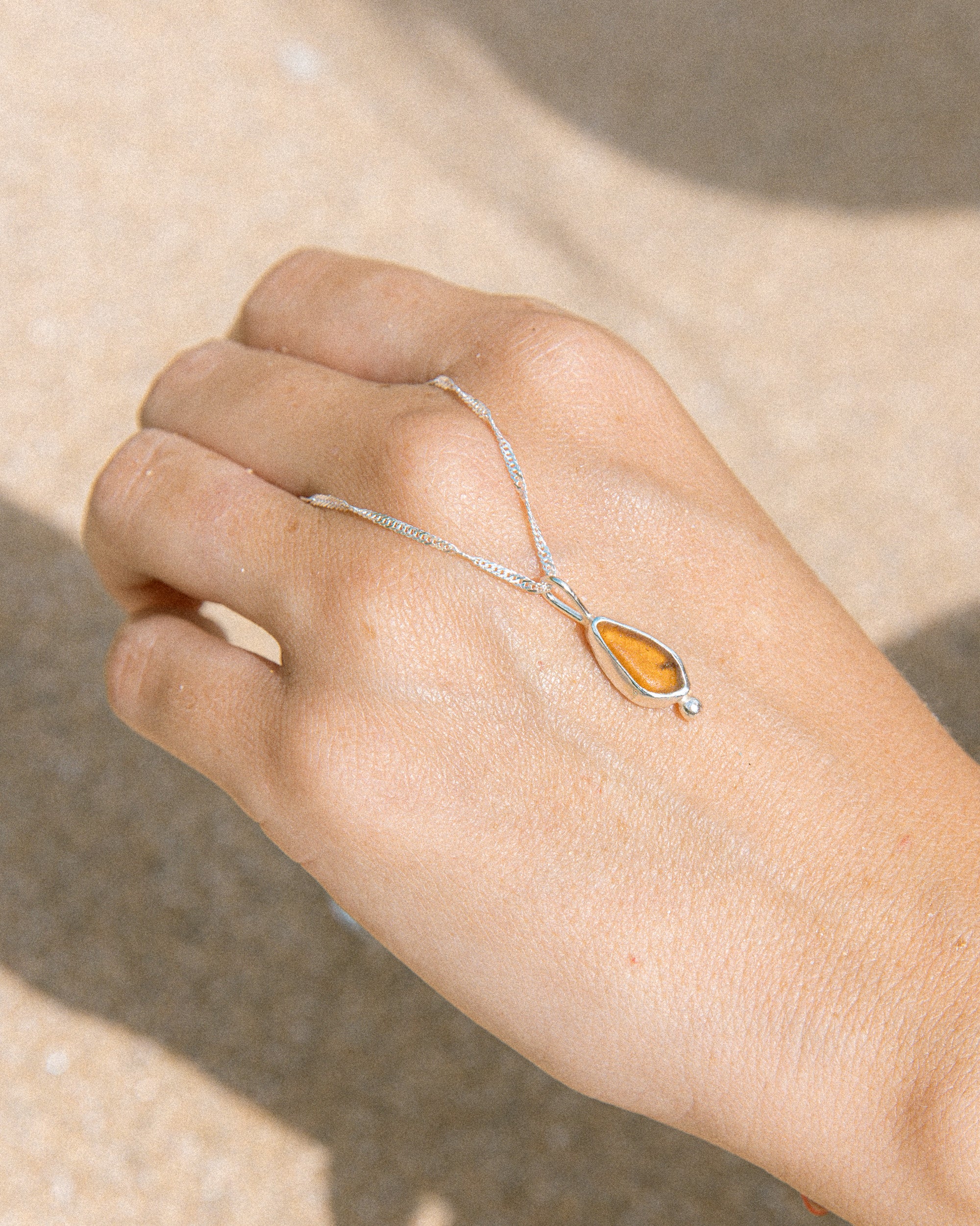 Amber sea glass necklace held in hand, handmade sterling silver, Broken Wave Jewellery Newquay

