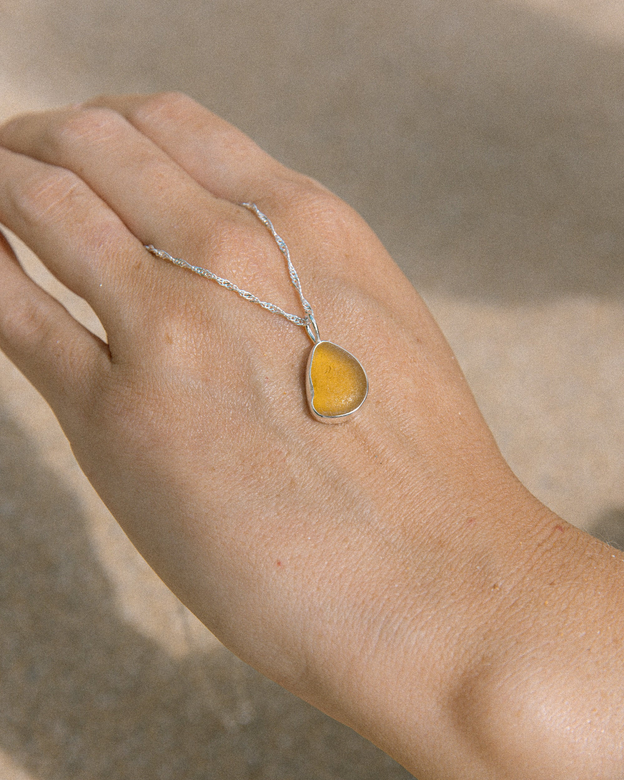 Honey yellow sea glass drop necklace in sterling silver on pale surface, Broken Wave Jewellery Cornwall
