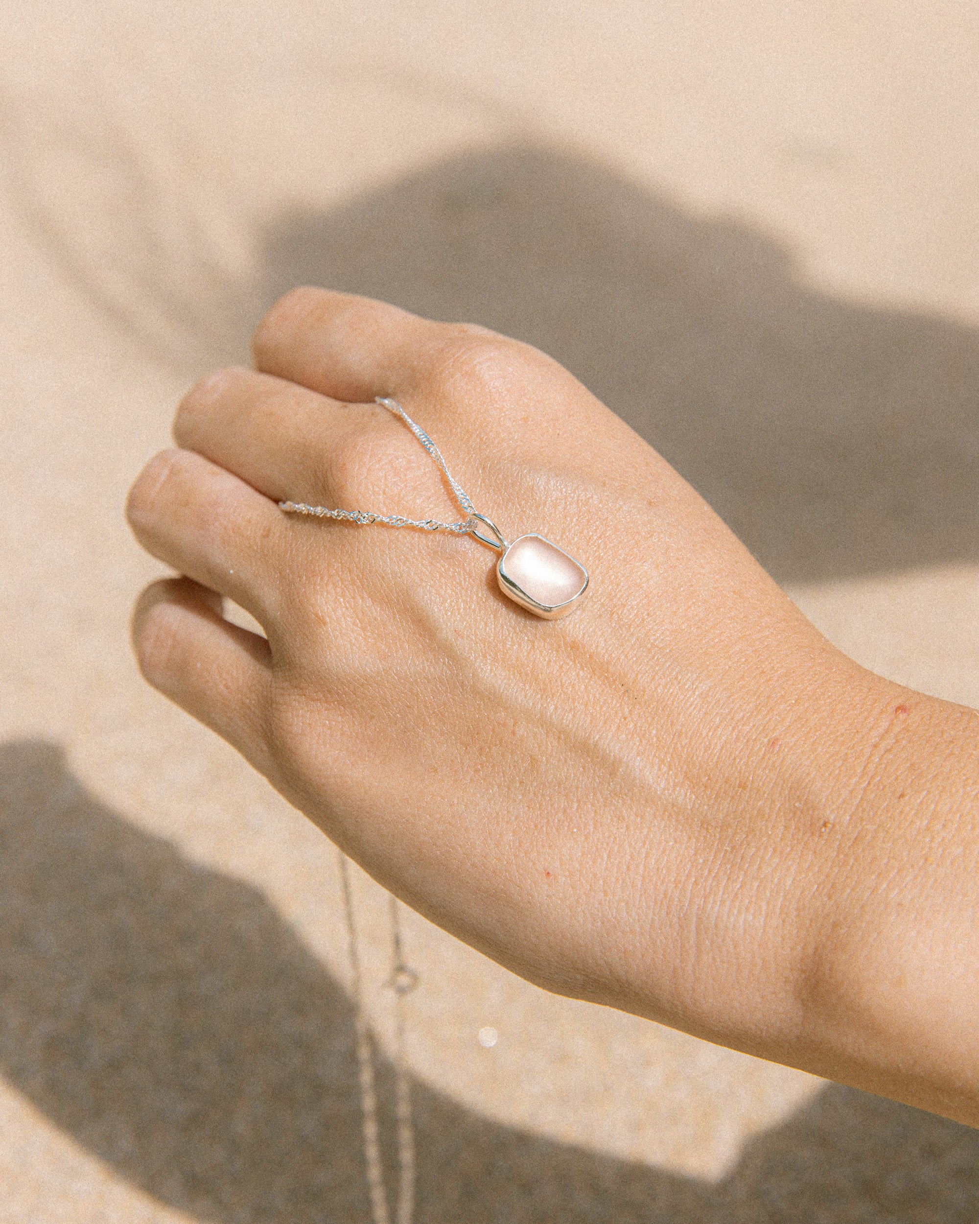 Pink sea glass necklace held in hand, handmade sterling silver, Broken Wave Jewellery Newquay
