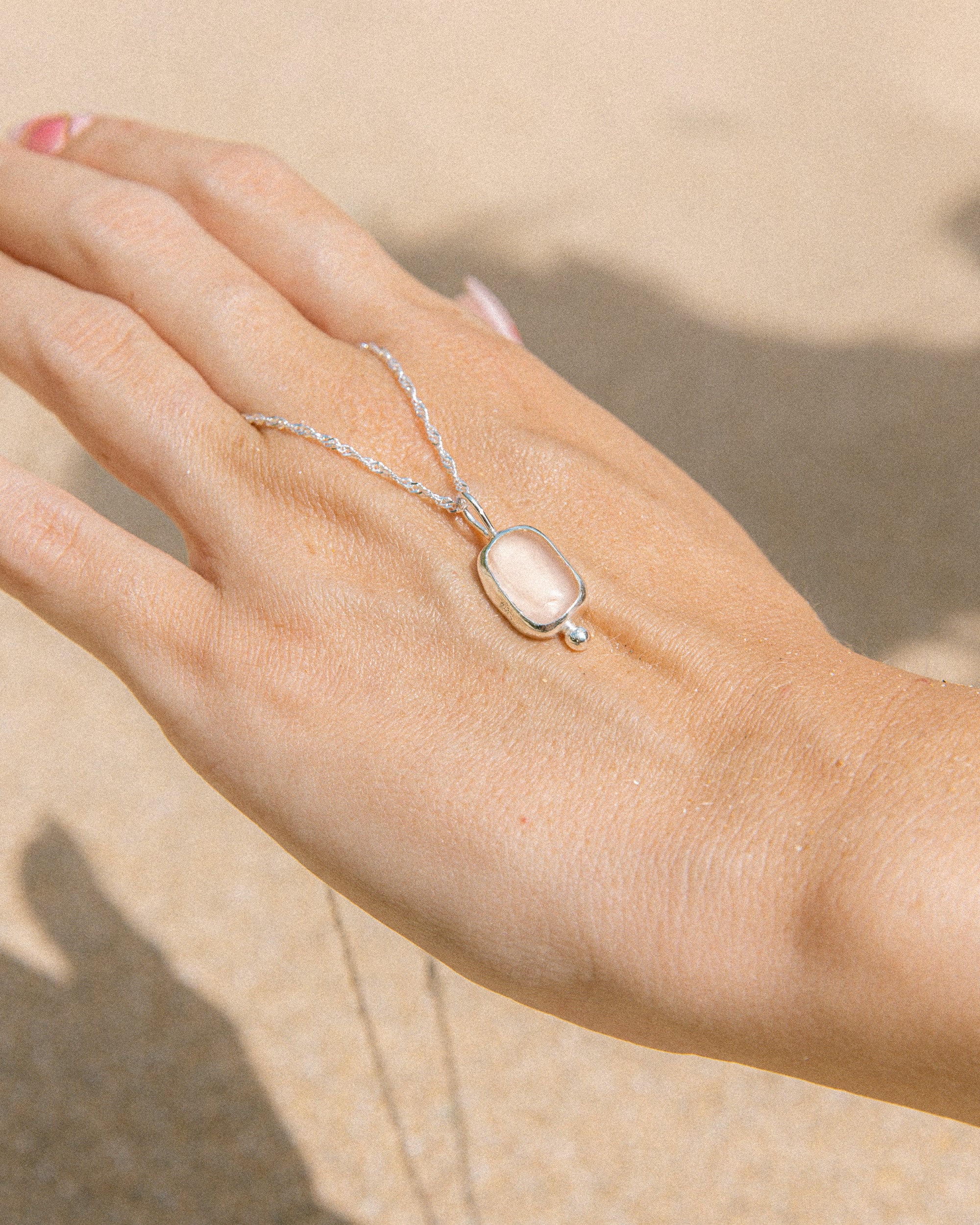 Pink sea glass necklace held in hand, handmade sterling silver, Broken Wave Jewellery Newquay
