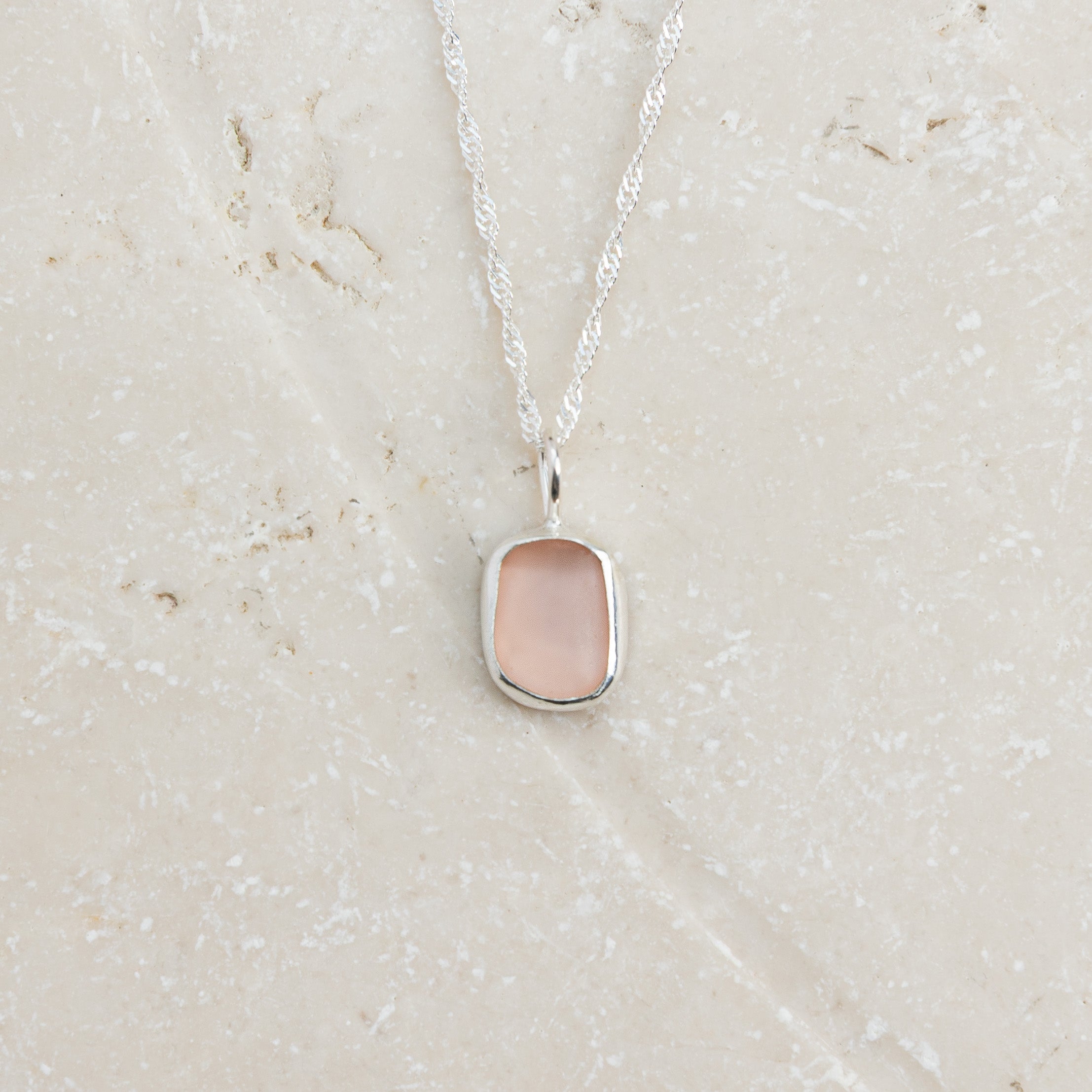 Rare pink sea glass necklace in sterling silver on sandy surface, Broken Wave Jewellery Cornwall
