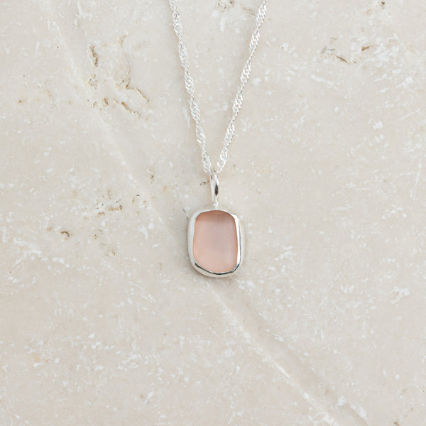 Rare pink sea glass necklace in sterling silver on sandy surface, Broken Wave Jewellery Cornwall
