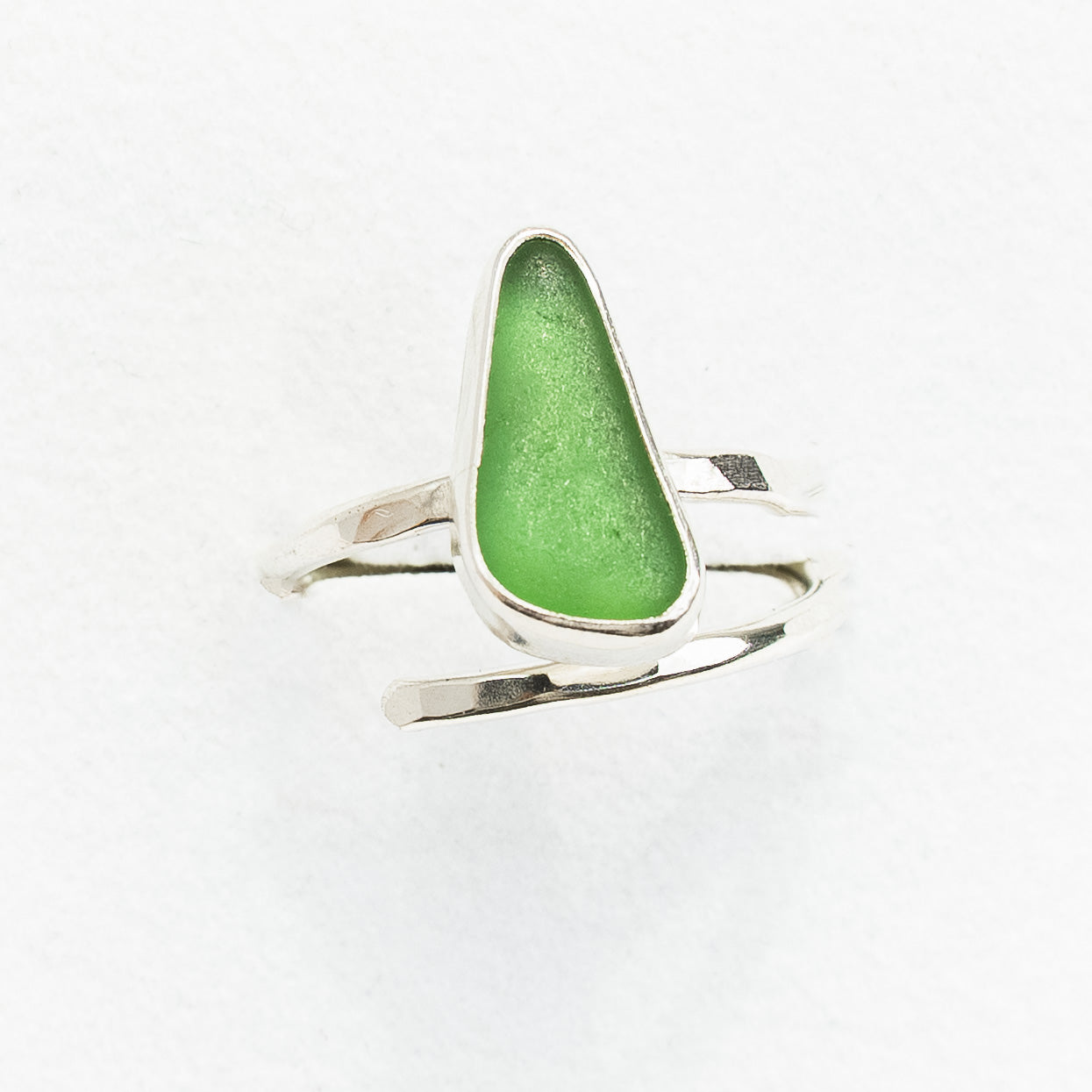 Green sea glass ring with silver band on a white background
