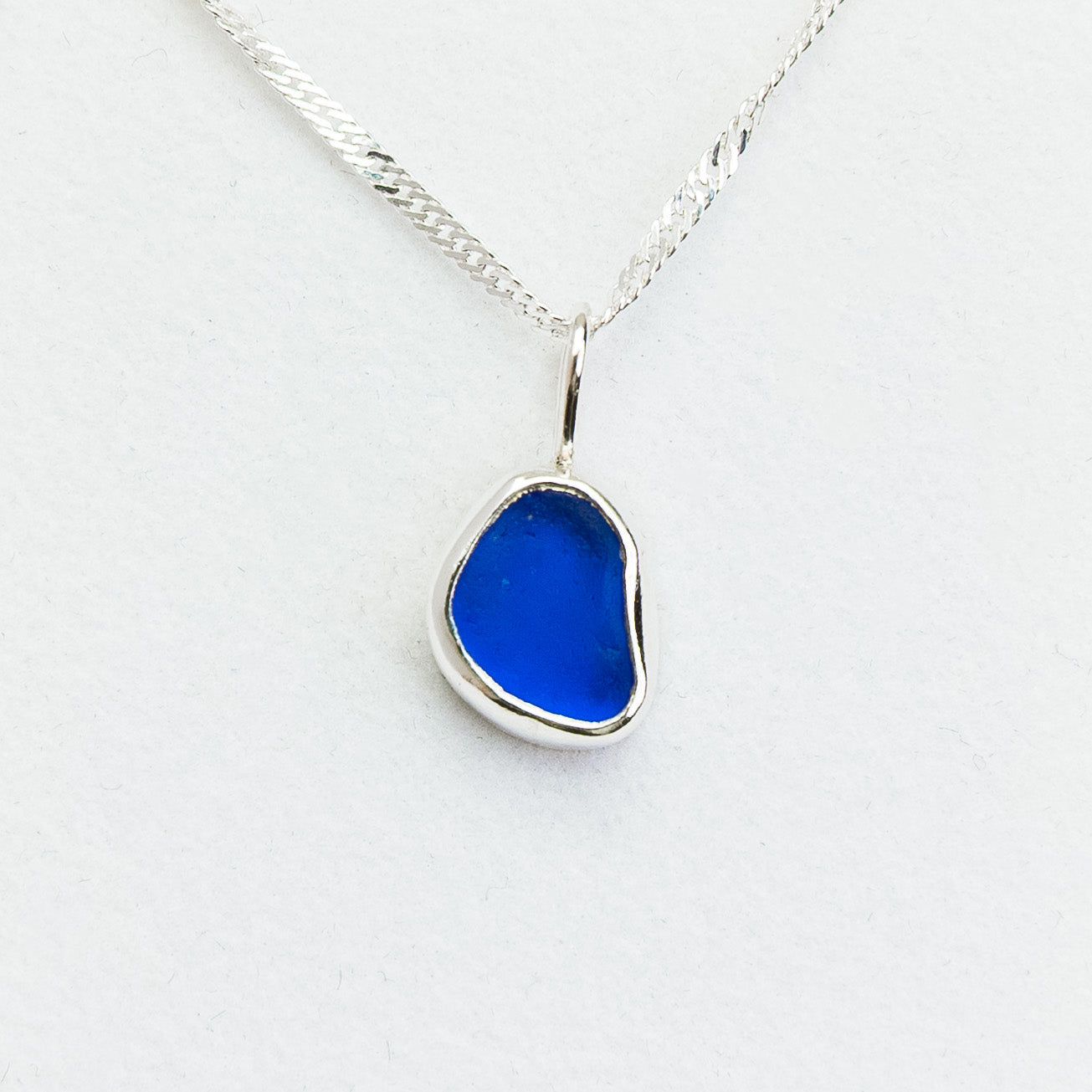 Blue sea glass pendant on a silver chain against a white background