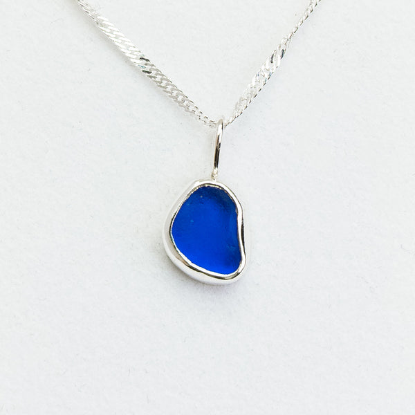 Blue sea glass pendant on a silver chain against a white background