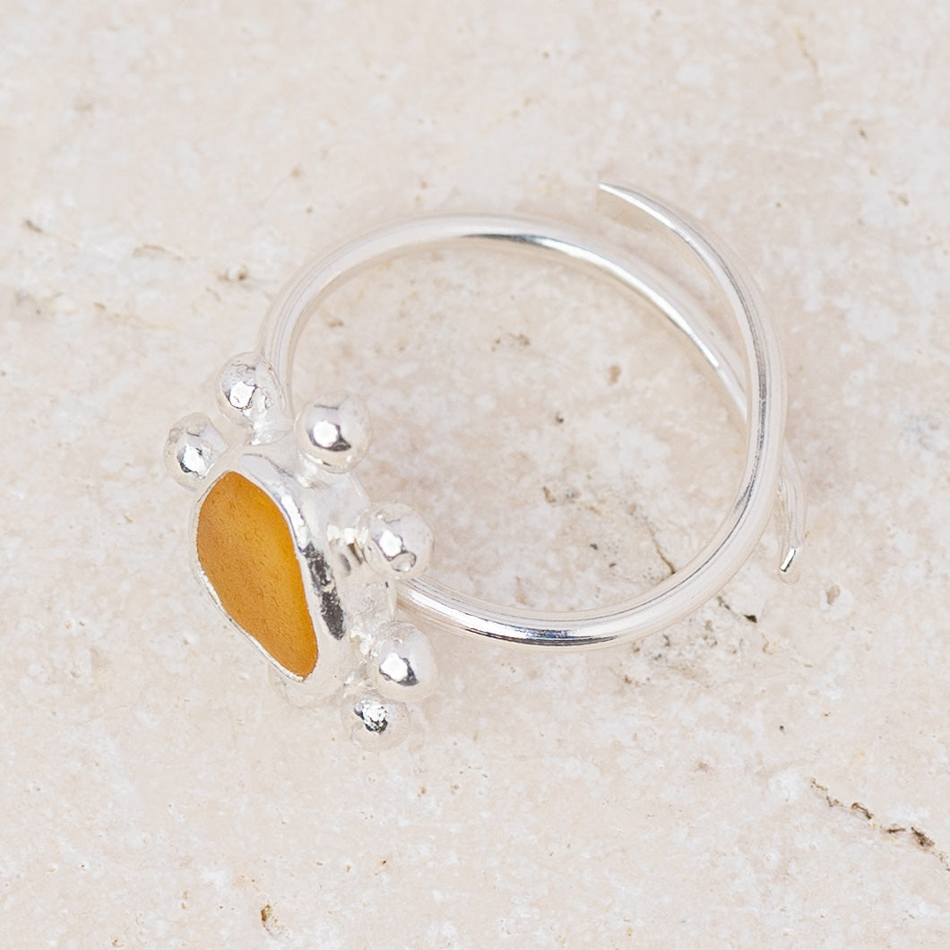 A sterling silver open-shank ring featuring a small paw print design with a polished yellow-gold heart-shaped center, displayed on a light beige textured stone surface.