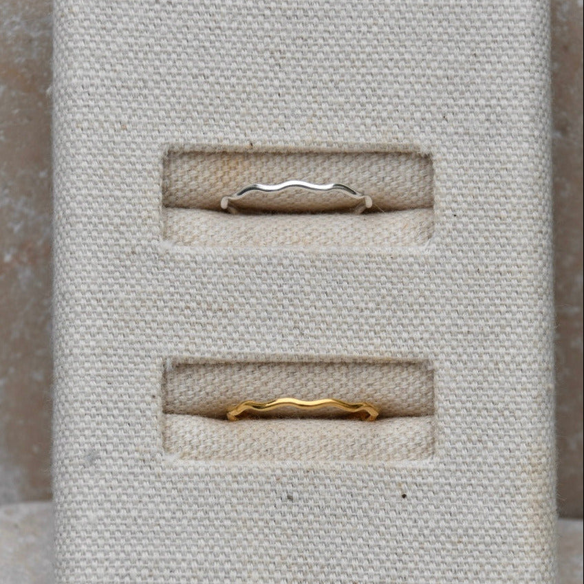 One gold and one silver ring displayed in a textured beige jewellery box against a neutral background