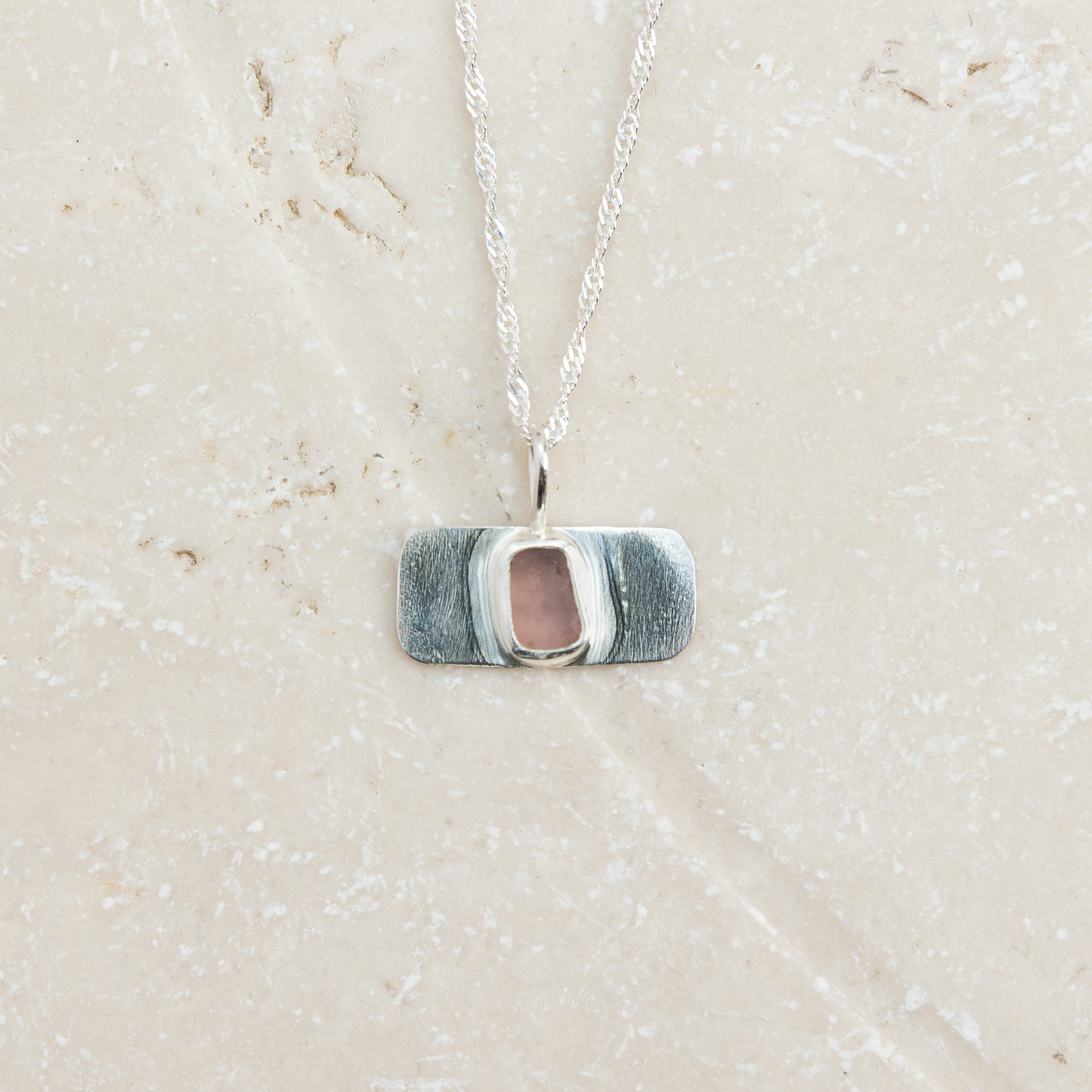 Rare purple sea glass necklace in sterling silver on pale sandy surface, Broken Wave Jewellery Cornwall

