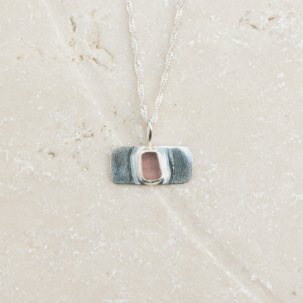 Rare purple sea glass necklace in sterling silver on pale sandy surface, Broken Wave Jewellery Cornwall
