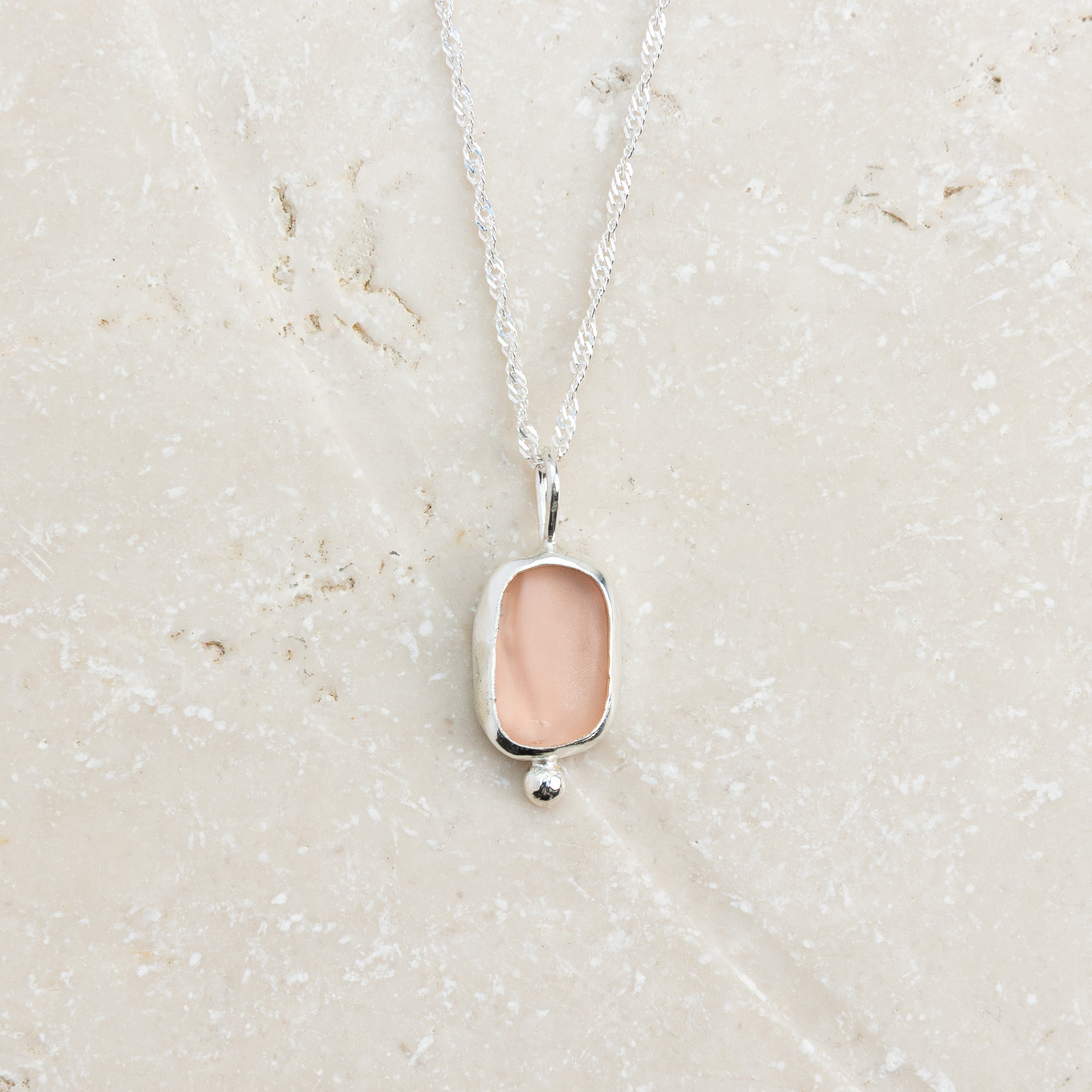 Rare pink sea glass necklace with silver ball detail on sandy surface, Broken Wave Jewellery Cornwall
