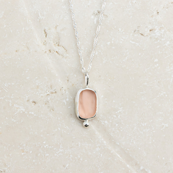 Rare pink sea glass necklace with silver ball detail on sandy surface, Broken Wave Jewellery Cornwall
