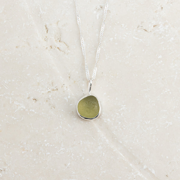 Citron green yellow sea glass necklace in sterling silver on pale surface, Broken Wave Jewellery Cornwall
