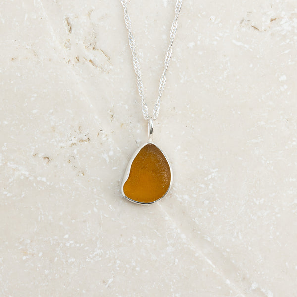 Honey yellow sea glass drop necklace in sterling silver on pale surface, Broken Wave Jewellery Cornwall
