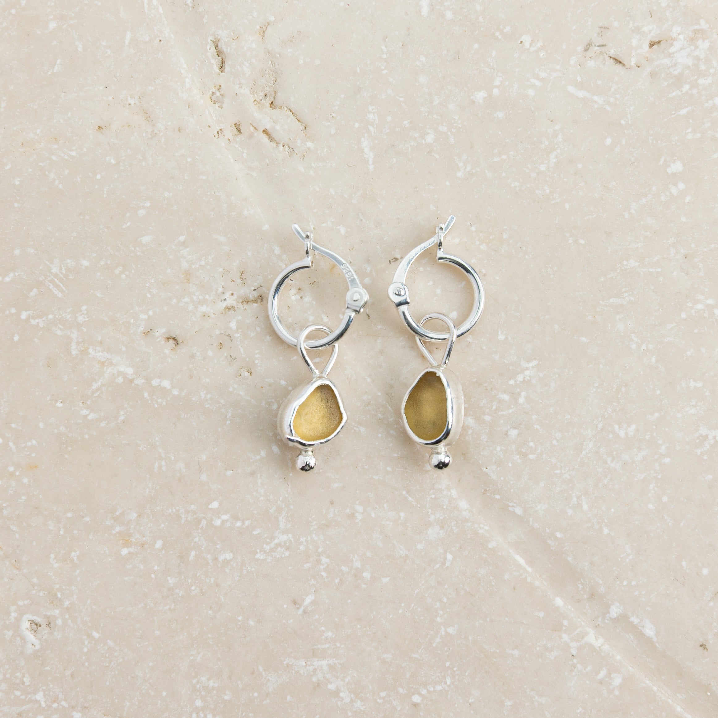 Yellow sea glass huggie earrings in sterling silver on sand, Broken Wave Jewellery Cornwall
