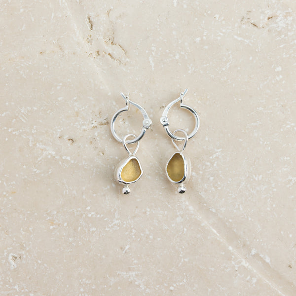 Yellow sea glass huggie earrings in sterling silver on sand, Broken Wave Jewellery Cornwall
