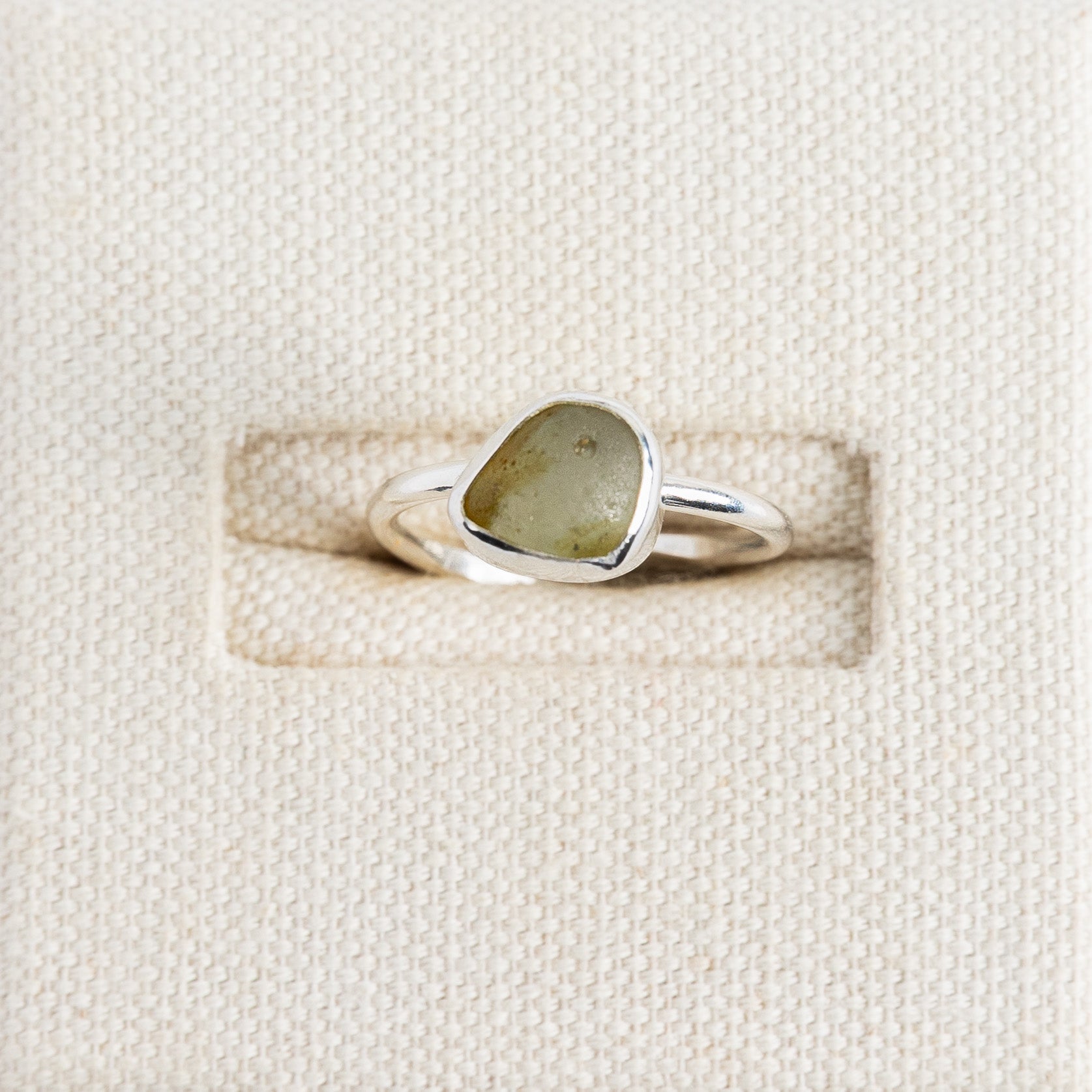 Olive green sea glass ring in sterling silver on textured white surface, Broken Wave Jewellery Cornwall
