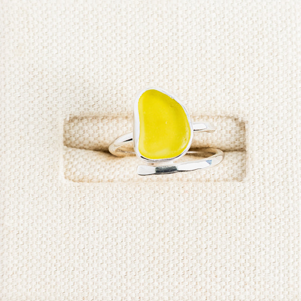 Bright yellow sea glass ring in sterling silver on textured white surface, Broken Wave Jewellery Cornwall

