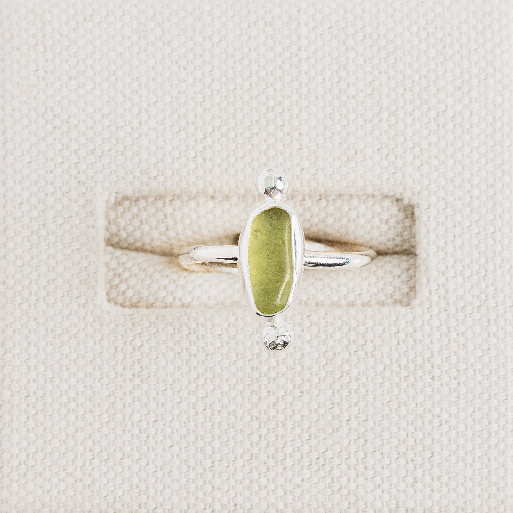 Lime yellow sea glass ring in sterling silver on textured white surface, Broken Wave Jewellery Cornwall