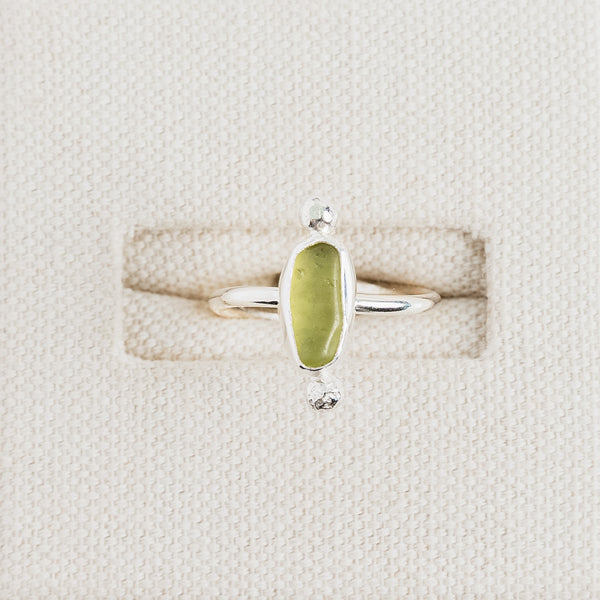 Lime yellow sea glass ring in sterling silver on textured white surface, Broken Wave Jewellery Cornwall