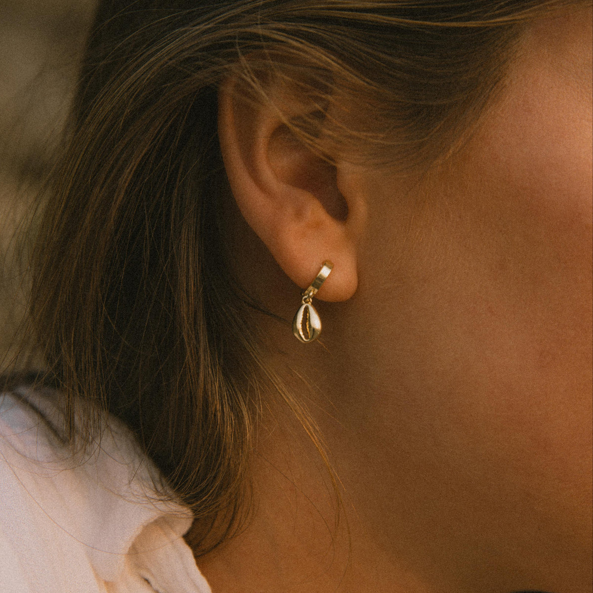 Close-up of a person wearing a gold earring with a blurred background